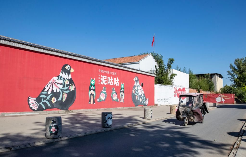 9月10日,在河南省浚县西杨玘屯村,村民从泥咕咕彩绘墙旁经过。新华社记者张帆 摄